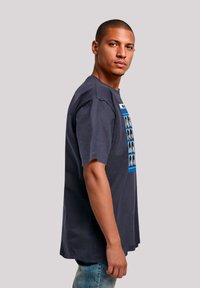 Gray, short-sleeve T-shirt featuring a graphic of faces in a grid with blue accents. Loose fit, cotton material, casual design.