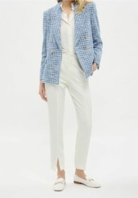 Světlomodrý tweedový blejzr se zlatými knoflíky, doplněný bílými kalhotami na míru s bočními rozparky a bílými loafry se zlatými detaily.