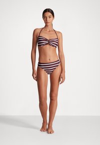 Bikini komplektas su bordo ir baltomis dryžiais. Viršus turi bandeau dizainą su centrinia auksine detale, o apačia yra klasikinio kirpimo.