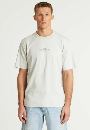 Light gray t-shirt with short sleeves, crew neck, and a small printed logo on the chest. Made of cotton, featuring a relaxed fit.