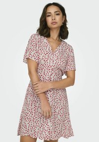Floral dress in light cream with a V-neckline, short sleeves, and a fitted waist. Red and green flower pattern throughout. Textured fabric.