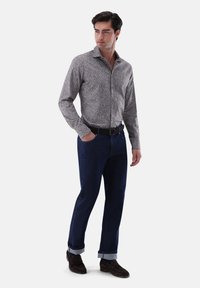 Fitted Hemd mit floralem Muster in Grautönen, kombiniert mit dunkelblauen Jeans, die an den Knöcheln umgekrempelt sind, und braunen Wildlederschuhen.