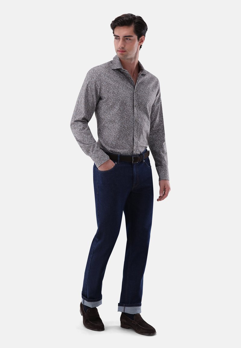Fitted Hemd mit floralem Muster in Grautönen, kombiniert mit dunkelblauen Jeans, die an den Knöcheln umgekrempelt sind, und braunen Wildlederschuhen.