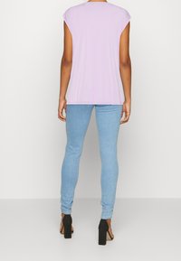 Kvinna iförd en lavendelfärgad kortärmad topp, ljusblå skinny jeans och svarta högklackade sandaler, sedd bakifrån.