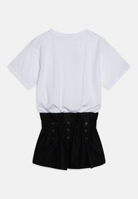 Černobílé šaty s bílým bavlněným tričkem nahoře a černou nasbíranou sukní s ozdobnými kovovými oky a skládaným designem.