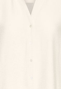 White button-up shirt featuring a subtle textured fabric, v-neckline, and five matching buttons down the front.