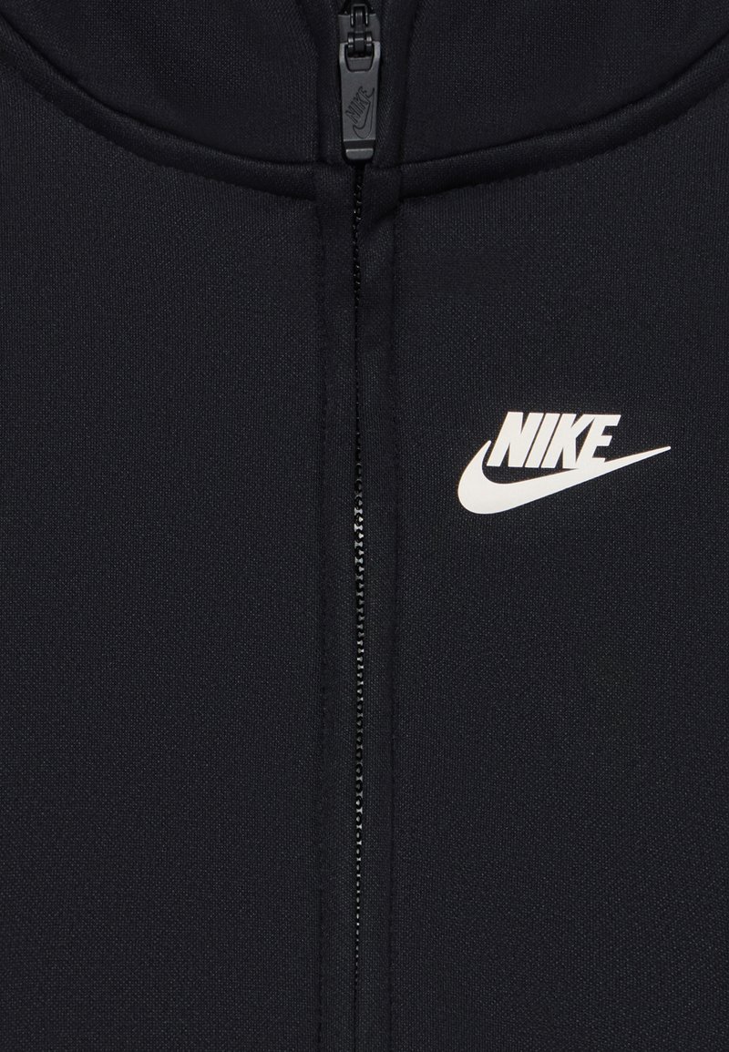 Schwarze Nike Zip-Up-Jacke aus strukturiertem Stoff mit hohem Kragen, versehen mit einem weißen Nike-Logo auf der oberen linken Seite.