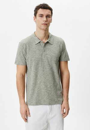 Camisa polo de manga corta en gris claro, con una tela texturizada, cuello clásico y botonera de tres botones. Diseño simple sin patrones.