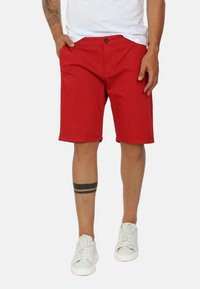 Shorts rossi in cotone con chiusura a bottone, tasche laterali e taglio dritto. Abbinati a sneakers bianche. Design semplice, senza fantasie.
