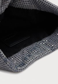 Kleine zilveren clutch van mesh met zwarte stoffen binnenkant en merklabel aan de binnenzijde, weergegeven vanuit een topzicht op een witte achtergrond.