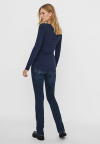 Haut à manches longues bleu marine en tissu lisse, associé à un jean foncé ajusté avec un design classique à cinq poches et des coutures subtiles.