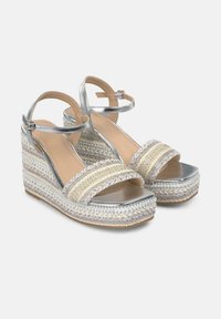Sandalias de cuña plateadas con diseño de paja trenzada, que cuentan con dos tiras anchas y una correa al tobillo. Detalles texturizados con acentos ornamentales.