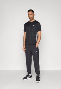 Camiseta deportiva negra con logo blanco, combinada con pantalones jogger negros que presentan un logo y franjas laterales. Completado con zapatillas deportivas negras.