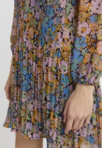 Pleated-mekko, jossa on monivärinen kukkakuosi vaaleanpunaisen, sinisen, vihreän ja oranssin sävyissä, valmistettu kevyestä, puoliläpinäkyvästä materiaalista.