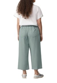 Lichtgroene linnen brede broek met een elastische band; gecombineerd met een losse witte t-shirt. Twee achterzakken zijn zichtbaar.