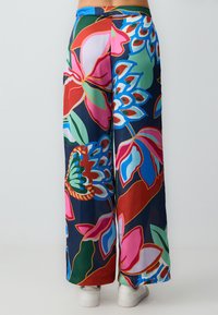 Kleurvolle, vloeiende broeken van lichtgewicht stof met een groot bloemenpatroon met roze, groene en blauwe details op een donkere achtergrond.