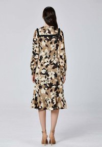 Robe midi florale beige avec des motifs noirs et blancs, manches longues, ourlet volanté et décolleté carré avec des accents noirs.
