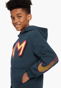 Felpa blu navy con tasca a marsupio, caratterizzata da una grande grafica "TM" multicolore e dal logo Nike a strisce gialle e rosa sulla manica.