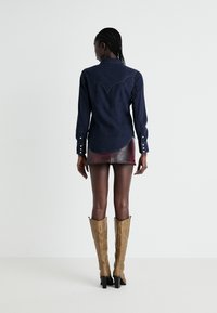 Ciemnoniebieska koszula dżinsowa z długimi rękawami, w westernowym stylu, z yoke i zapięciami na guziki, zestawiona z burgundową mini spódnicą i beżowymi kozakami do kolan.