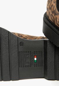 Chaussures en daim à imprimé léopard avec une semelle en caoutchouc noir. Les détails notables comprennent une texture en relief et une étiquette "Fabriqué en Italie" avec un drapeau tricolore.