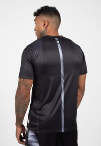 Zwarte sportieve shirt met korte mouwen, voorzien van een gradiënt stippenpatroon op de schouders en een centrale zilveren verticale streep.