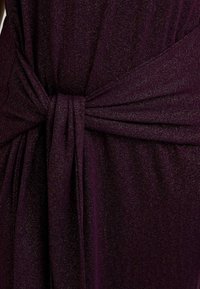 Tessuto di abito viola con una finitura scintillante e testurizzata. Presenta una cintura annodata in vita e drappeggi morbidi, enfatizzando un design elegante.