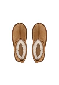 Bottes chelsea en suede marron avec une douce doublure en fourrure blanche, présentant un motif cousu et une languette pour un enfilage facile.