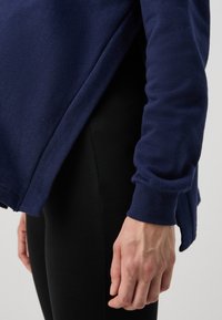 Sudadera navy con un corte relajado, que presenta aberturas laterales y mangas largas. Combinada con leggings negros. Textura suave visible.