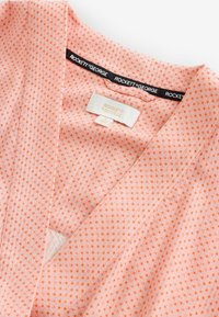 Indumento rosa chiaro con pois arancioni, scollo a V e etichetta del marchio "Rockett St George" sul colletto e sull'etichetta interna.