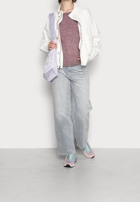 Vit bomberjacka, vinröd texturerad tröja, ljusgrå vida jeans och pastellfärgade sneakers med svart sula. Lila axelväska.