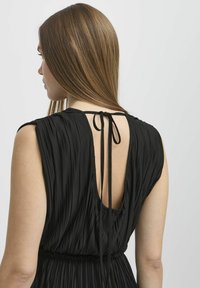 Abito nero a pieghe con scollatura profonda sulla schiena e dettaglio annodato al collo, che mette in mostra un tessuto morbido e texture e vita elastica.
