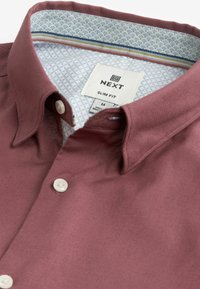 Burgundi színű, slim-fit ing gomb leeresztett gallérral. A bélés világoskék mintás, kontrasztos csíkos díszítéssel.