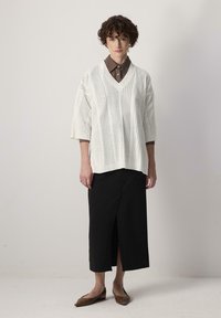 Pull en tricot blanc surdimensionné avec un col en V et des côtes verticales, associé à une jupe mi-longue noire avec une fente devant, et des ballerines marron.