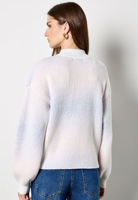 Pastelkleurige geribbelde trui met een hoge hals, oversized mouwen en een relaxte pasvorm. Gecombineerd met blauwe denim jeans.