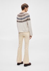 Πλεκετό πουλόβερ σε κρέμα με σχέδιο στο γύρο λαιμό σε σκούρο γκρι και μπλε. Συνδυασμένο με κρέμα φαρδιά παντελόνια και καφέ μποτάκια ankle.