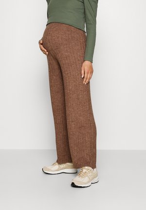 Brune ribbede bukser med bred benstørrelse, kombinert med en grønn langermet topp og beige joggesko. Glatt tekstur.