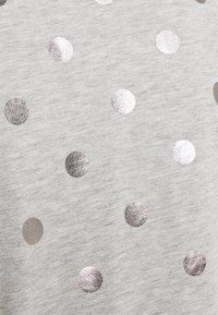 Heller grauer Stoff mit gleichmäßig verteilten, metallisch silbernen und grauen Punkten, der eine weiche Textur und ein lässiges Design aufweist.