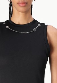 Svart ribbet ermeløs topp med metalliske detaljer, inkludert kjeder og ringer på skulderen for ekstra pynt.