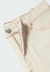 Vaqueros de mezclilla beige con costuras naranjas, con cremallera frontal y cierre de broche. La tela es texturizada con un acabado suave.