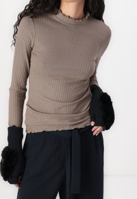 Ribbade långärmade toppar i taupe med en volangkrage; kombinerad med svarta fingerlösa handskar med fluffiga detaljer. Marinblå byxor med en bred knytning.