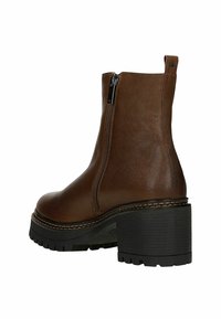 Hnědá kožená kotníková bota se zapínáním na boční zip, robustním černým podpatkem, texturovanou podrážkou a viditelnými švy.