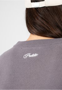 Pull en maille gris avec un col à côtes et un logo brodé blanc dans le dos. Texture douce avec un motif subtil et uniforme.