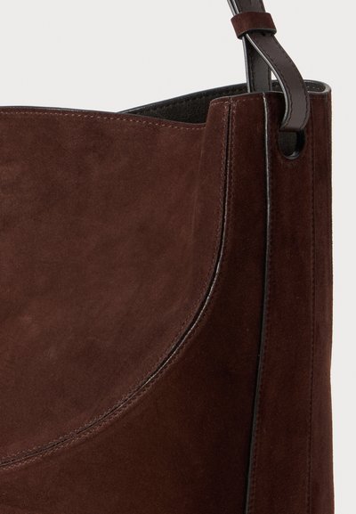 Brown suede shoulder bag with a smooth texture, featuring a curved design and contrasting stitching, and a leather strap with a metal accent.