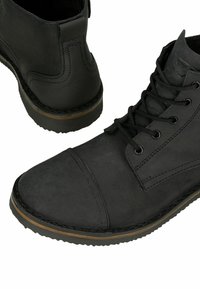 Stivali ankle in pelle nera con finitura liscia, suola in gomma, tacco texturizzato e design con lacci e occhielli in metallo.