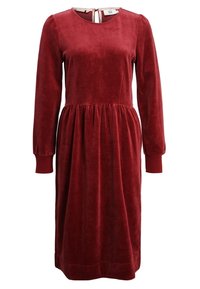Szkarłatna aksamitna sukienka z długimi rękawami, okrągłym dekoltem i marszczoną talią. Posiada zapięcie na plecach w kształcie dziurki oraz dopasowane mankiety.