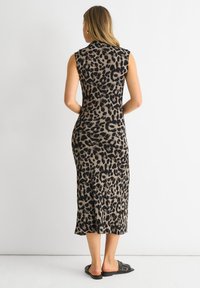 Leopard print, sleeveless, form-fitting dress in tan and black, knee-length with a straight hem. Worn with black slide sandals.