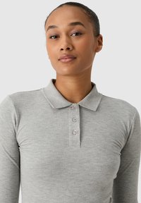 Szary prążkowany golf z kołnierzykiem, z trzema guzikami. Materiał wydaje się miękki i dopasowany. Brak widocznych wzorów lub akcentów.