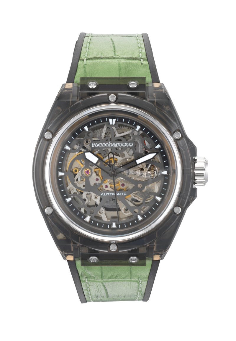 Rannekello, jossa on läpinäkyvä kuori, musta kellotaulu, hopeiset viisarit ja vihreä krokotiilikoimalla työstetty nahkaremmi. Hopeiset yksityiskohdat.