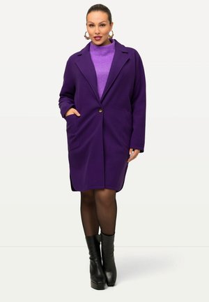 Langer lila Mantel mit eingekerbten Revers, Ein-Knopf-Verschluss, zwei vorderen Taschen, kombiniert mit einem lila Pullover und schwarzen Stiefeletten.