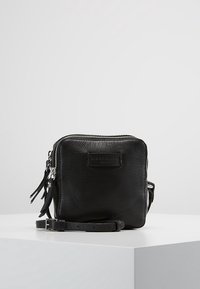 Borsa a tracolla nera in pelle con superficie texturizzata, chiusura a zip, tracolle removibili e un piccolo patch con logo sulla parte anteriore.